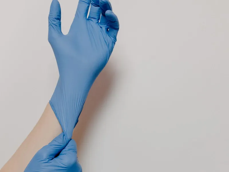 Blue-gloved hand with the cuff being adjusted; illustrative photography, not a grade identification.