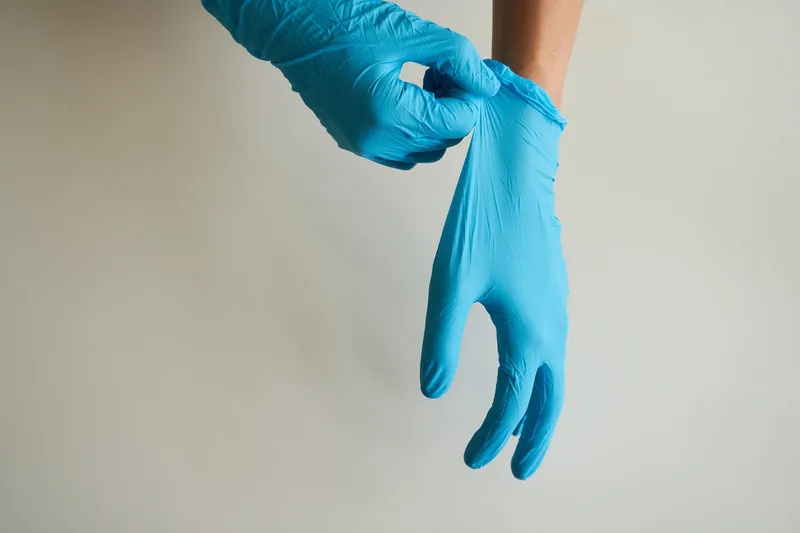 Close-up of hands adjusting a blue disposable glove against a light background.