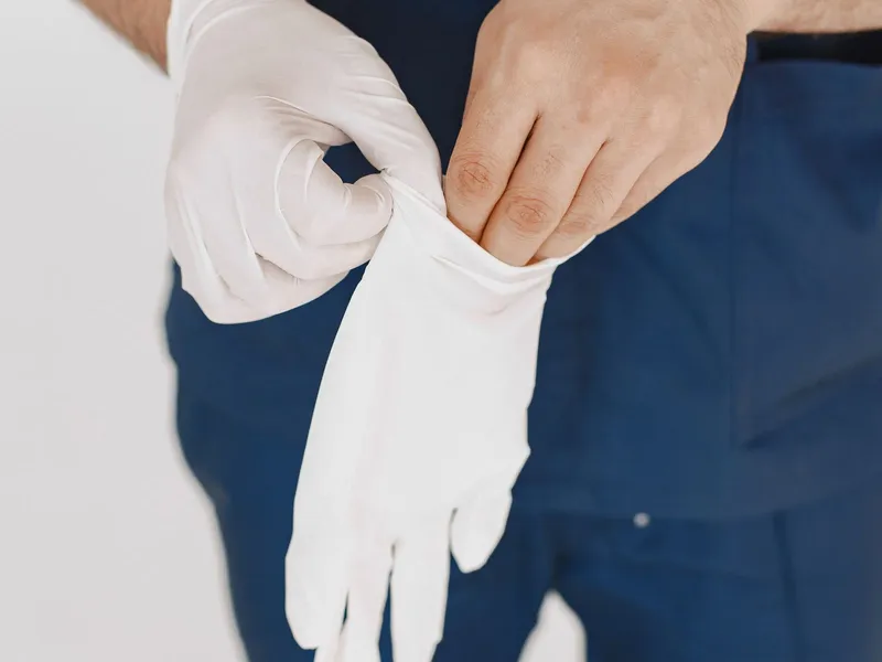 Hands adjusting a light-coloured disposable glove; illustrative glove-use photography.