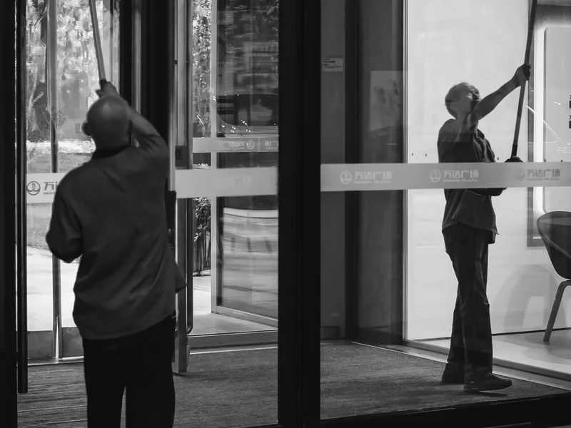 Janitors cleaning glass doors in an office building; illustrative facility-care photography.