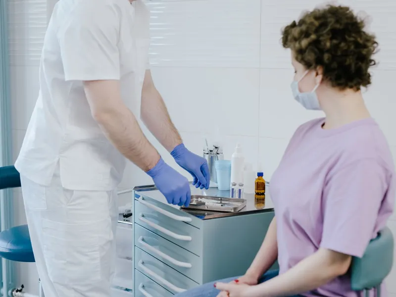 Gloved clinician preparing instruments beside a seated patient; illustrative clinical setting.